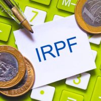 The initials IRPF written in blue color on a small piece of paper. Pen and Calculator in composition. Brazilian economy, income tax.